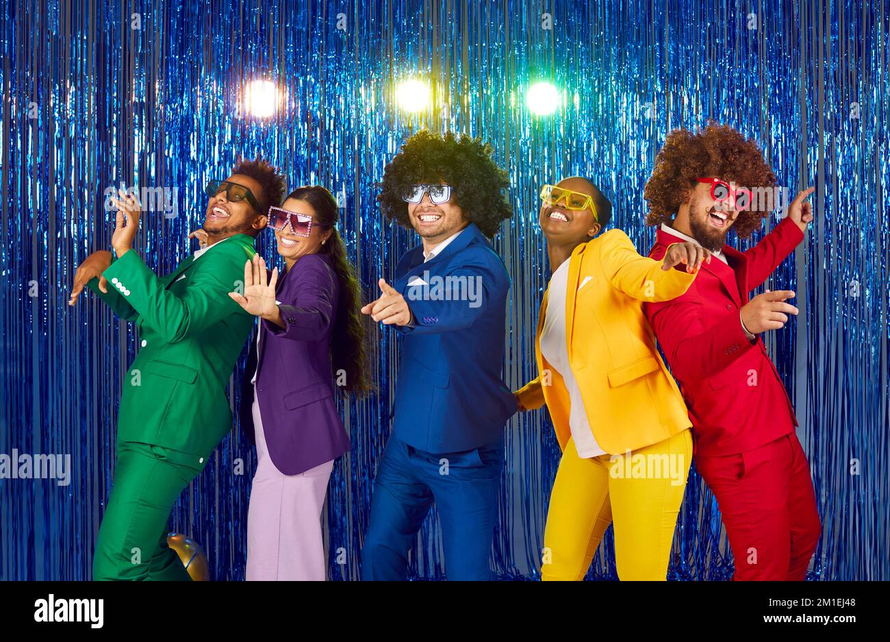 Funny people in colorful suits, wigs and disco glasses dancing and having fun at party Stock Photo