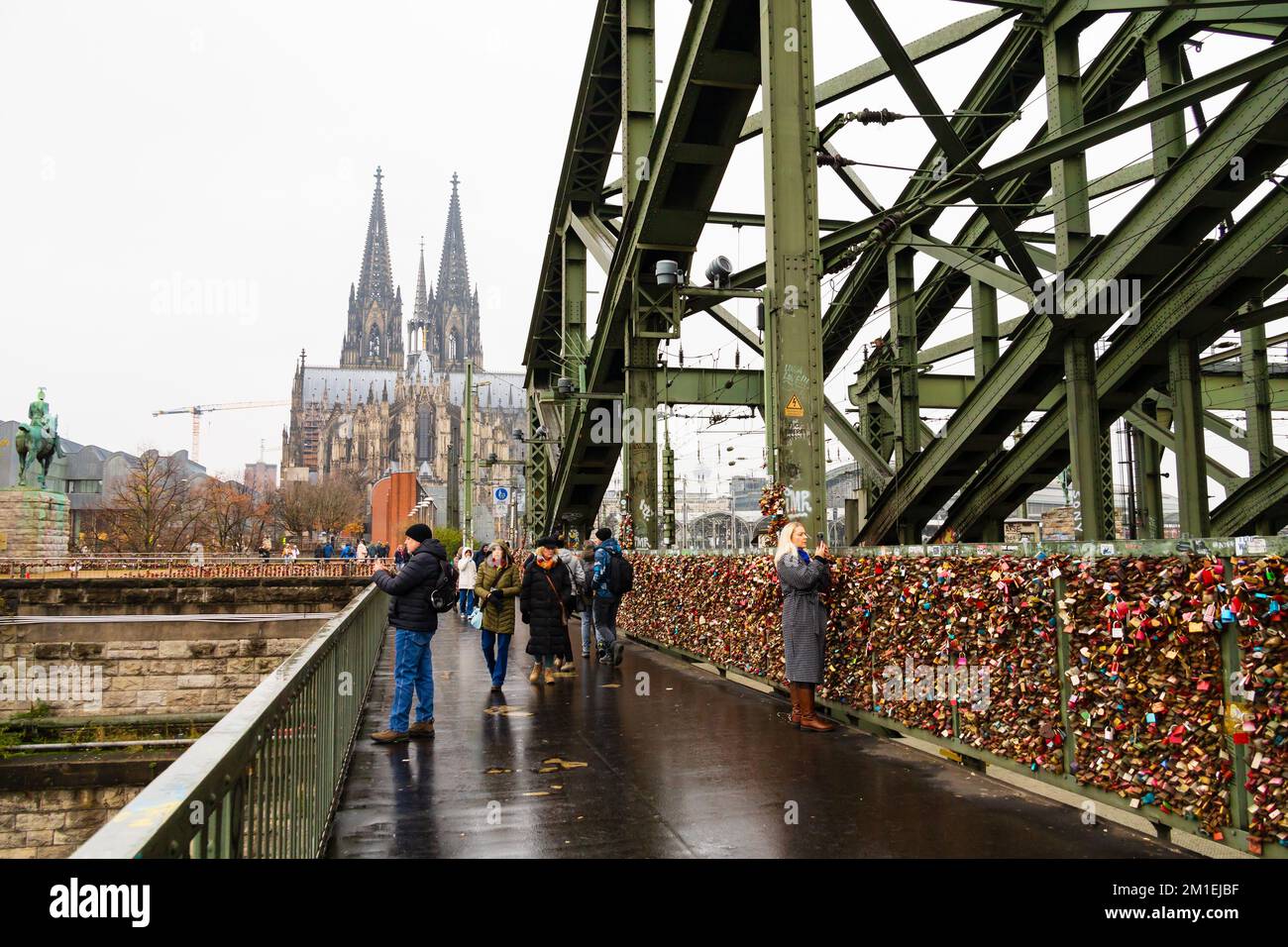 Pedestrians with a View of Koln Cologne cathedral Dom, from the Hohenzollernbrucke, Hohenzollern bridge, Germany. The railings are covered in love loc Stock Photo
