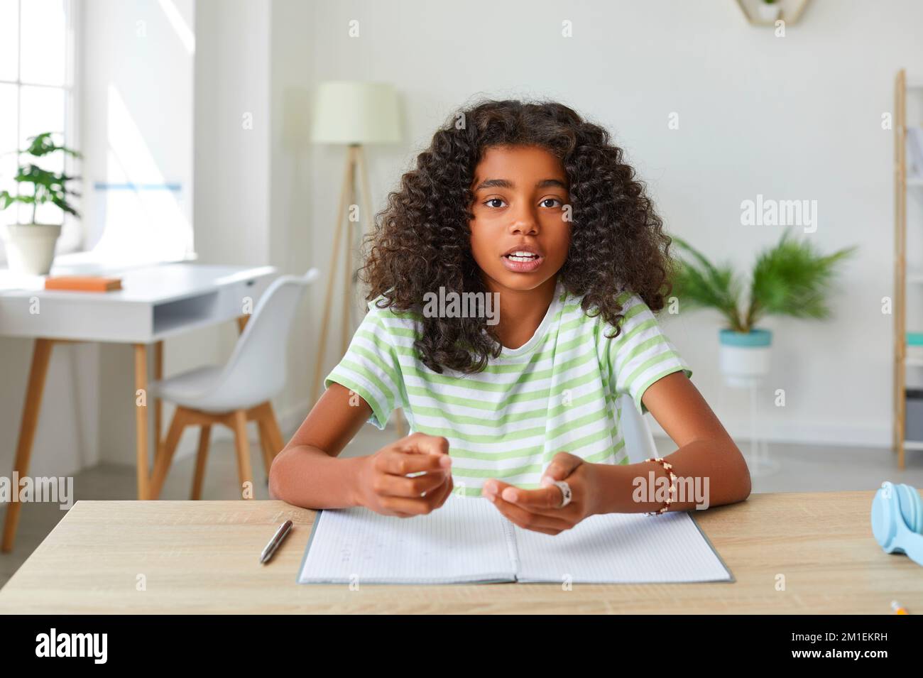 Talking african american teen girl is studying online looking at camera sitting at desk at home. Stock Photo