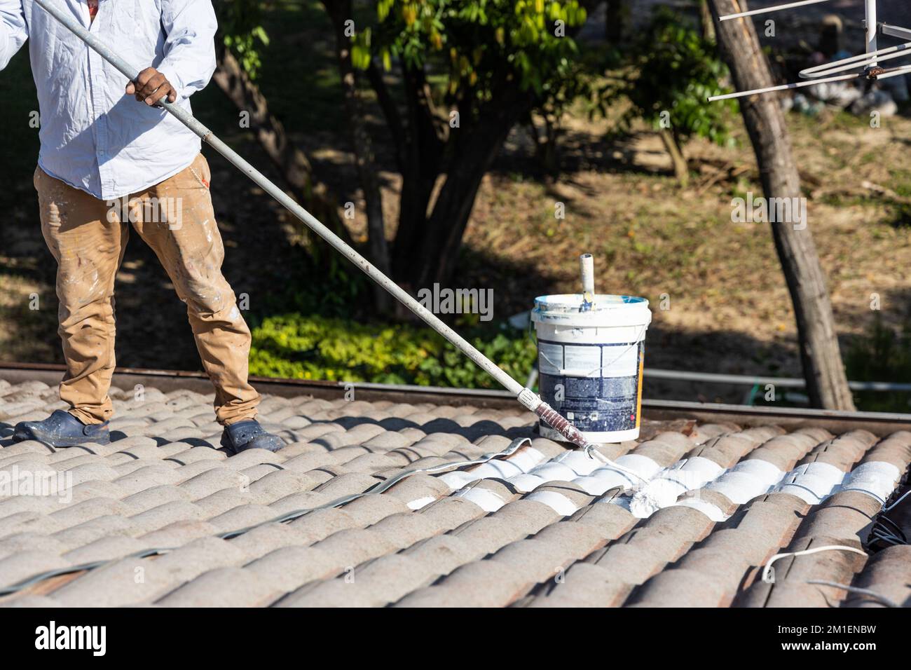 Worker adding undercoat foundation paint onto rooftop with roller at