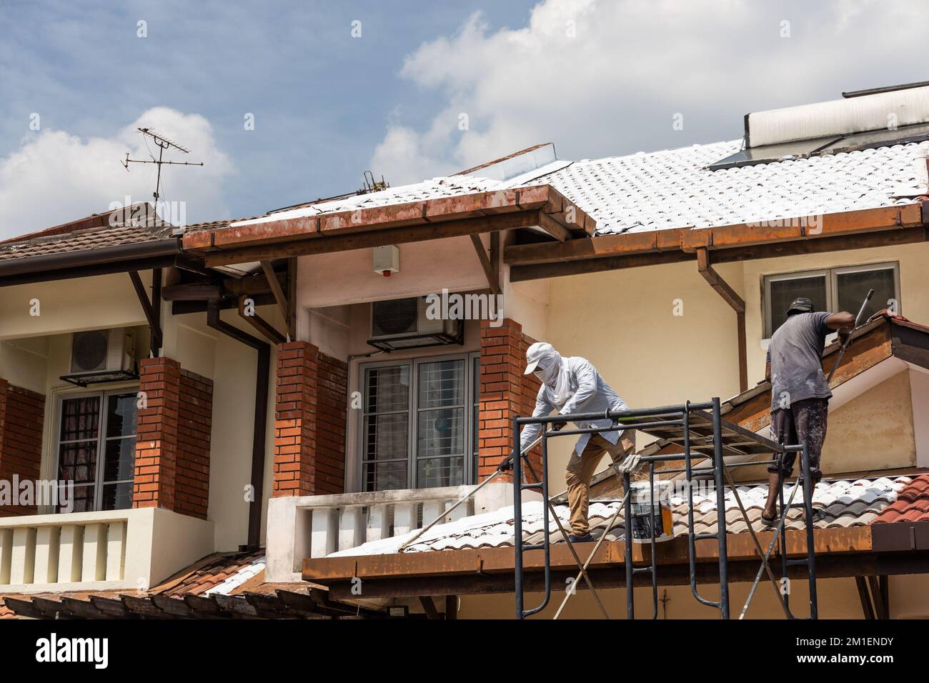 Worker adding undercoat foundation paint onto rooftop with roller at
