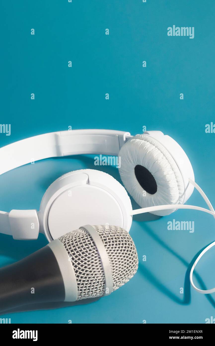 White headphones and scenic microphone on a blue background. vertical banner Stock Photo