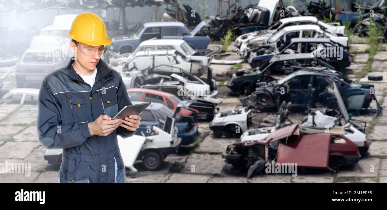 A worker with a digital tablet at a car recycling plant. Waste management concept Stock Photo