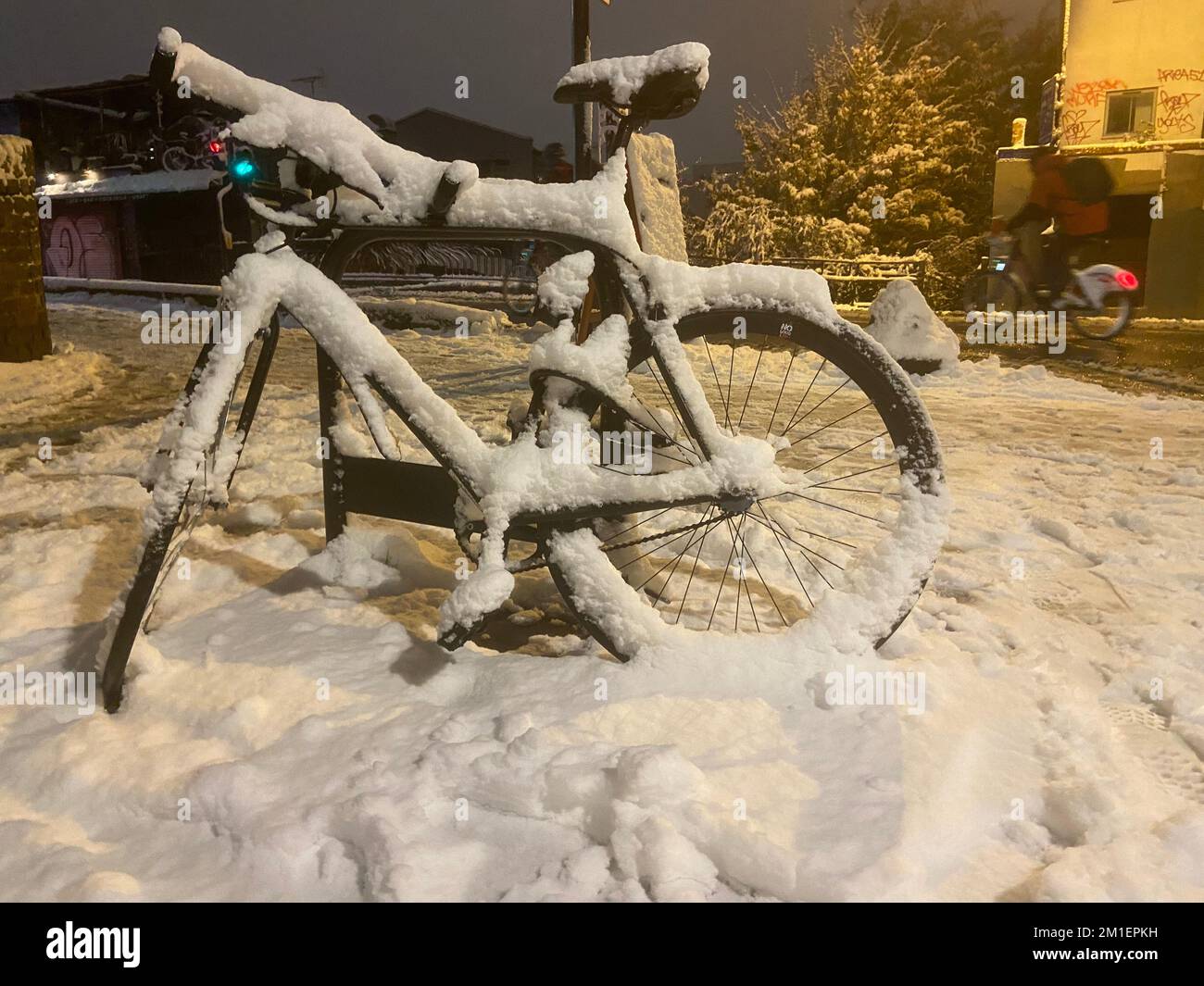Bicycle parked and snow covered and a commuter cyclist, cycling along Kingsland Road, East London after the snow storm Stock Photo