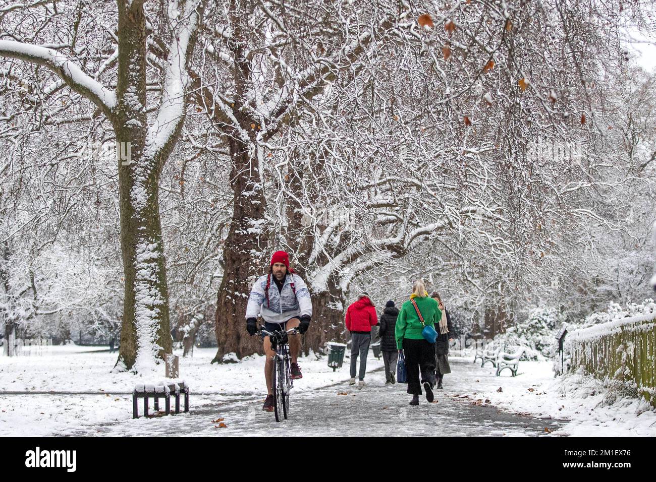 A person cycling and people walking in Kennington Park, London. Snow and ice have swept across parts of the UK, with cold wintry conditions set to continue for days. Picture date: Monday December 12, 2022. Stock Photo