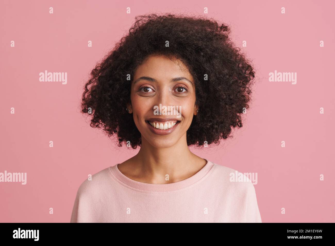 Black happy woman with afro hairstyle smiling and looking at camera isolated over pink background Stock Photo