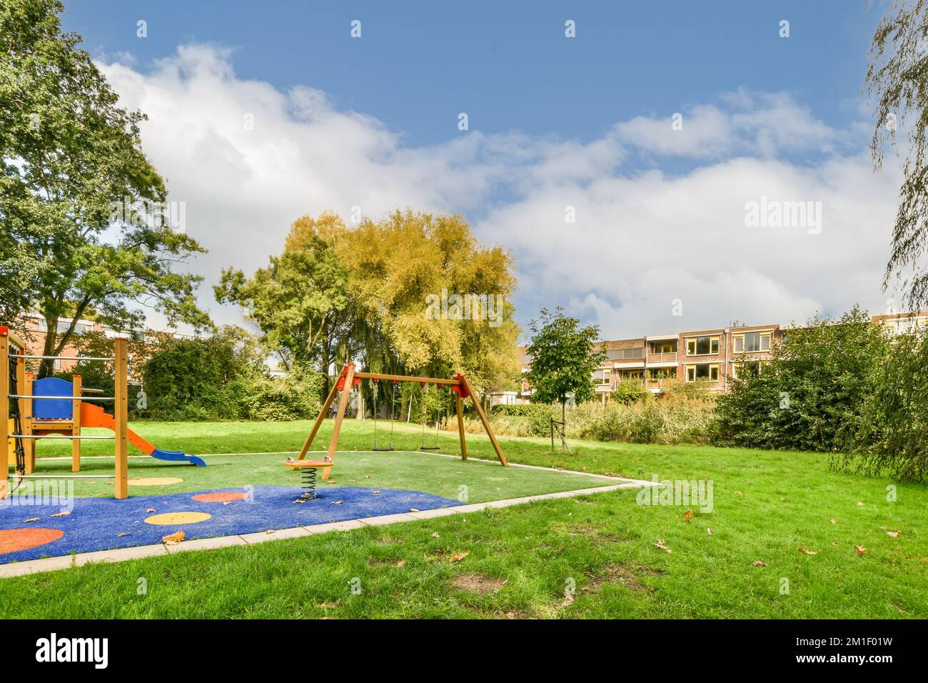 an outdoor play area with swings, slides and climbing equipment in the background is a blue sky filled with white clouds Stock Photo
