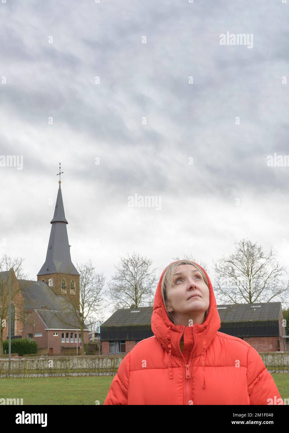 Chance of rain. A woman in a red hooded jacket looks up at the stormy sky. Place for text Stock Photo