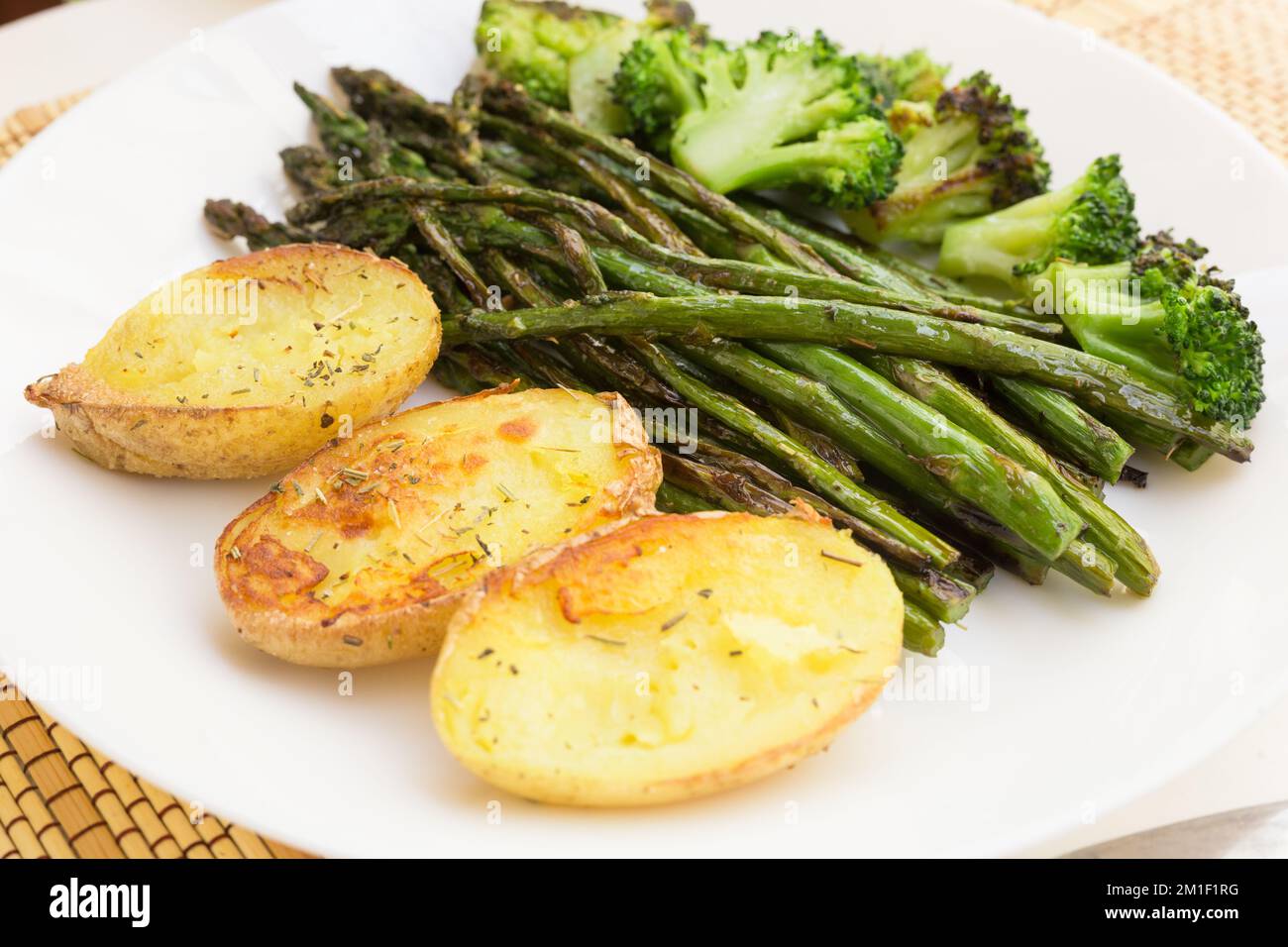lean dish of cooked fried inflorescences of broccoli, asparagus growth and baked potatoes and Provencal herbs Stock Photo