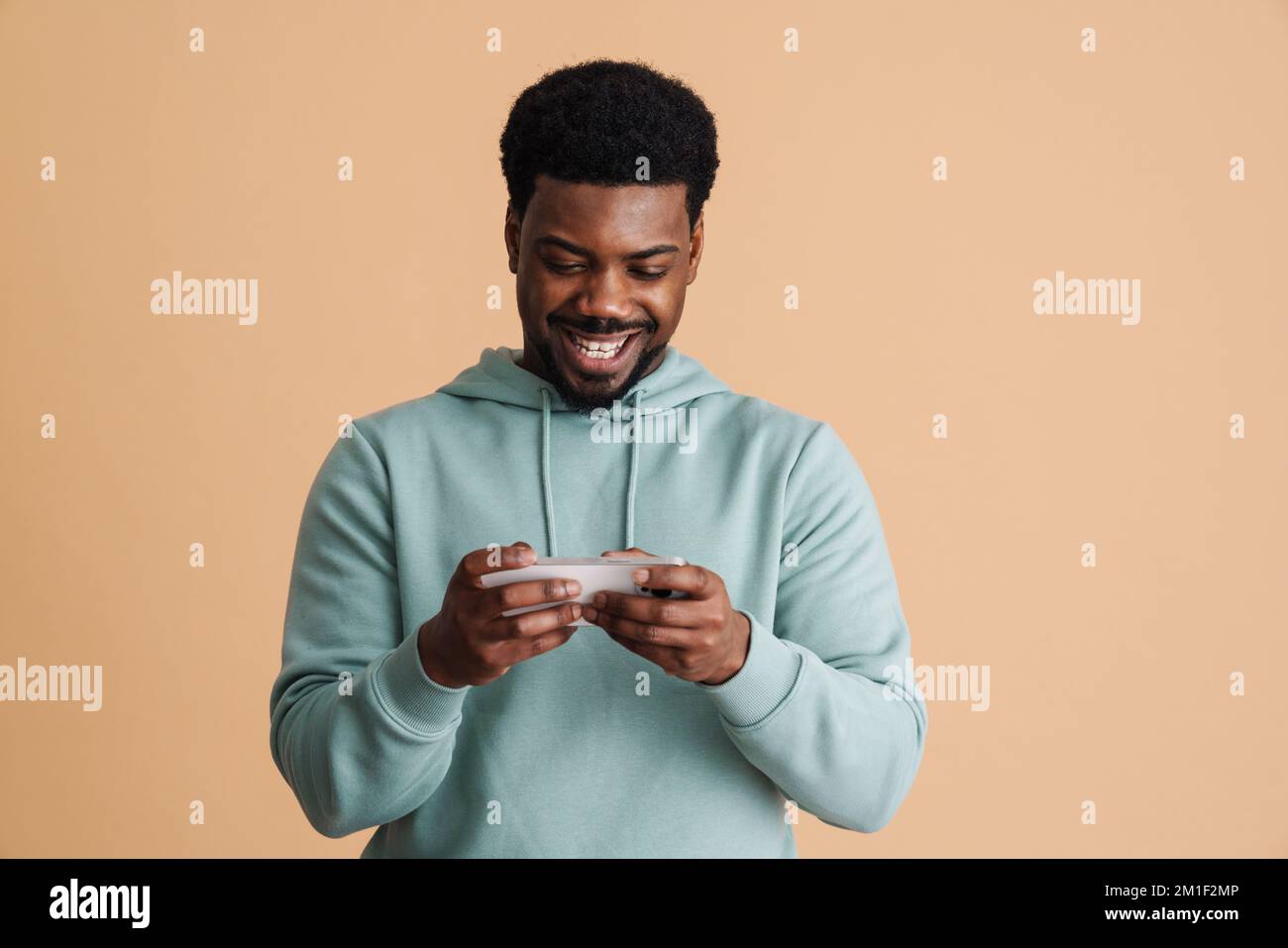 Black bearded young man smiling and using cellphone isolated over beige background Stock Photo