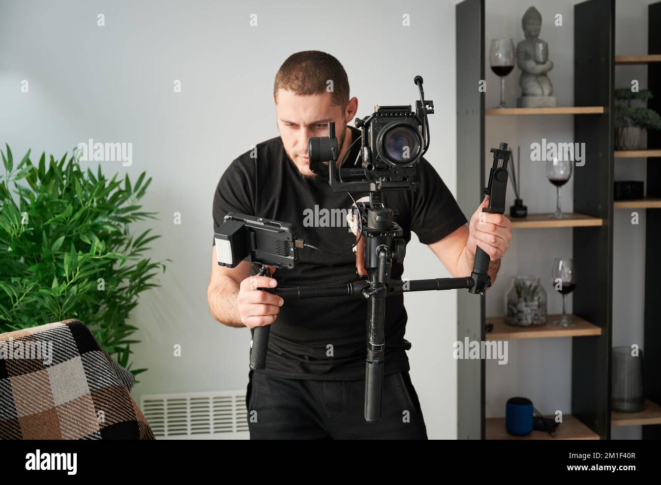 Videographer man shooting footage indoors, using camera mounted on gimbal stabilizer equipment. Stock Photo