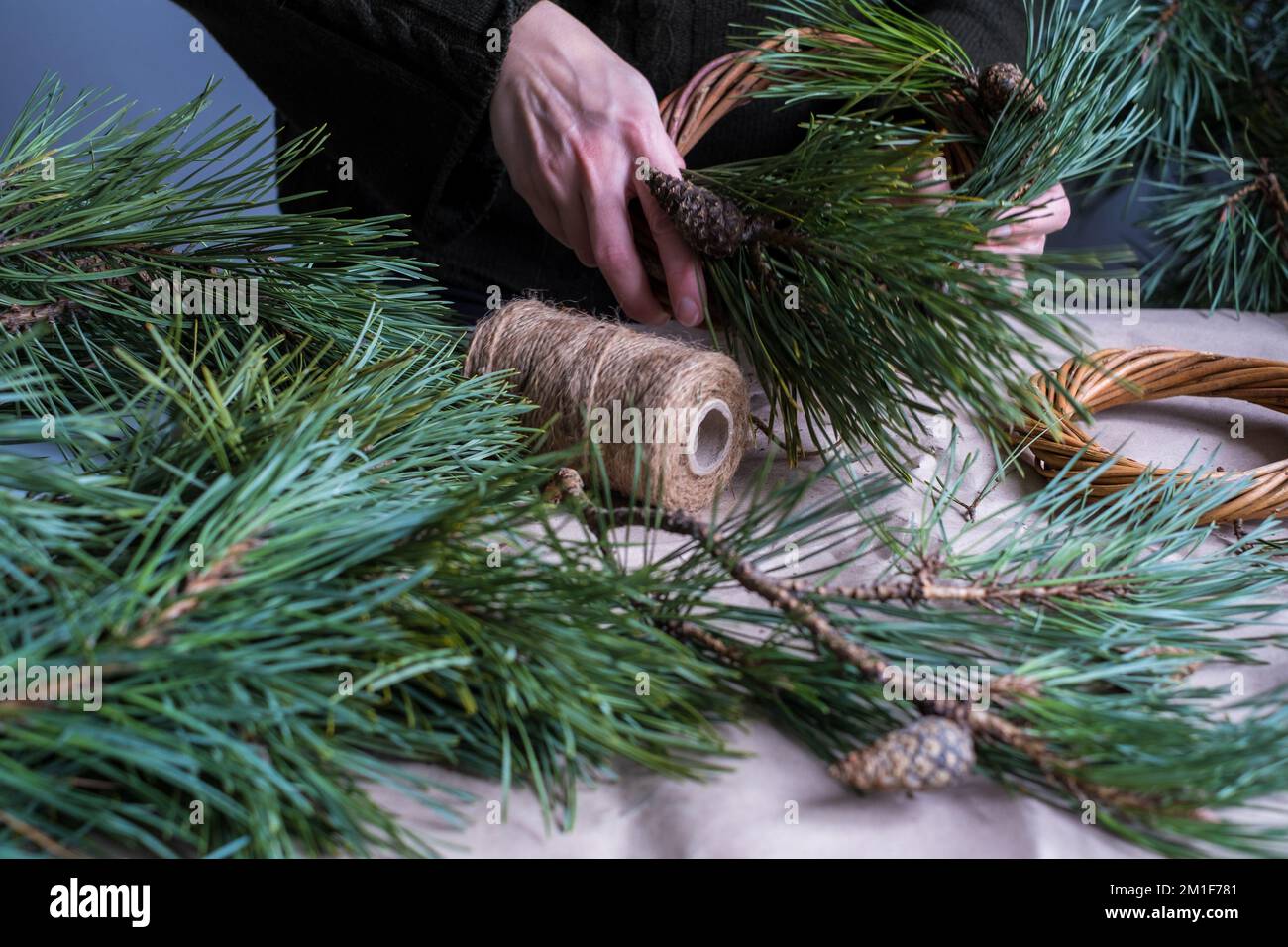 Making rustic Christmas wreath. Female hands on background of  wooden table with pine tree branches, cones, lights.Holiday preparations Stock Photo