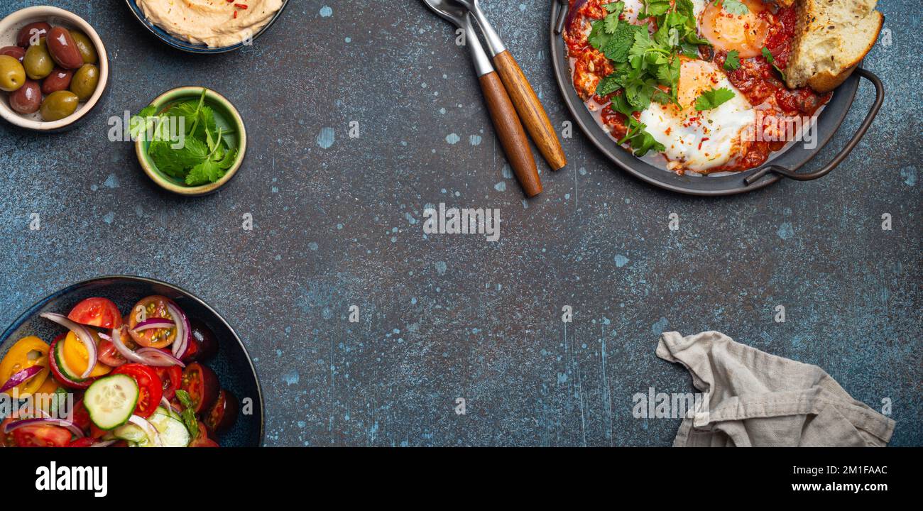 Middle Eastern breakfast or brunch with Shakshouka, toasts, vegetables salad, hummus, olives copy space Stock Photo
