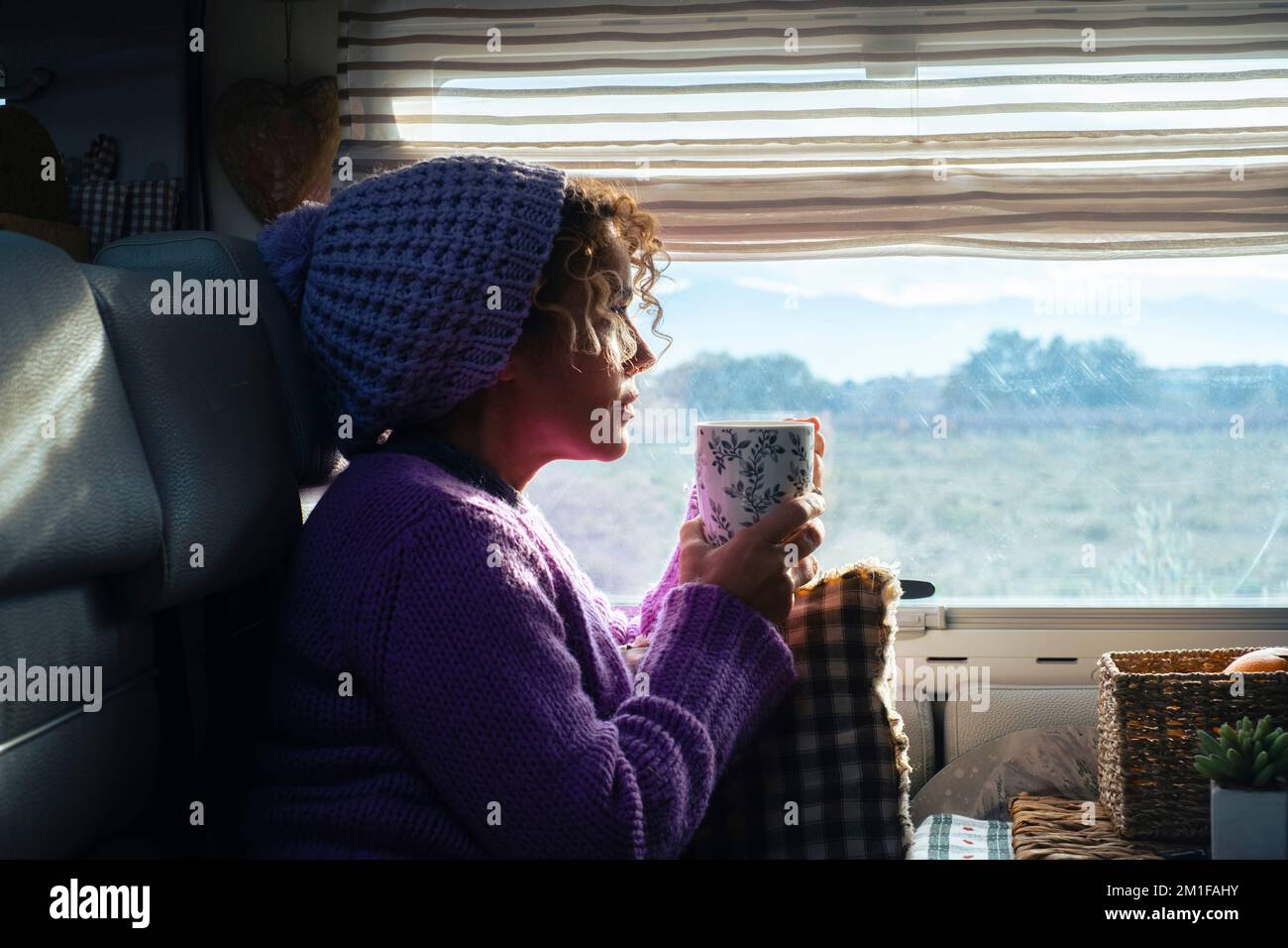 Side view of a woman drinking herbal tea having relax and chill moment inside her camper van looking the outdoor landscape in the parking. Travel noma Stock Photo