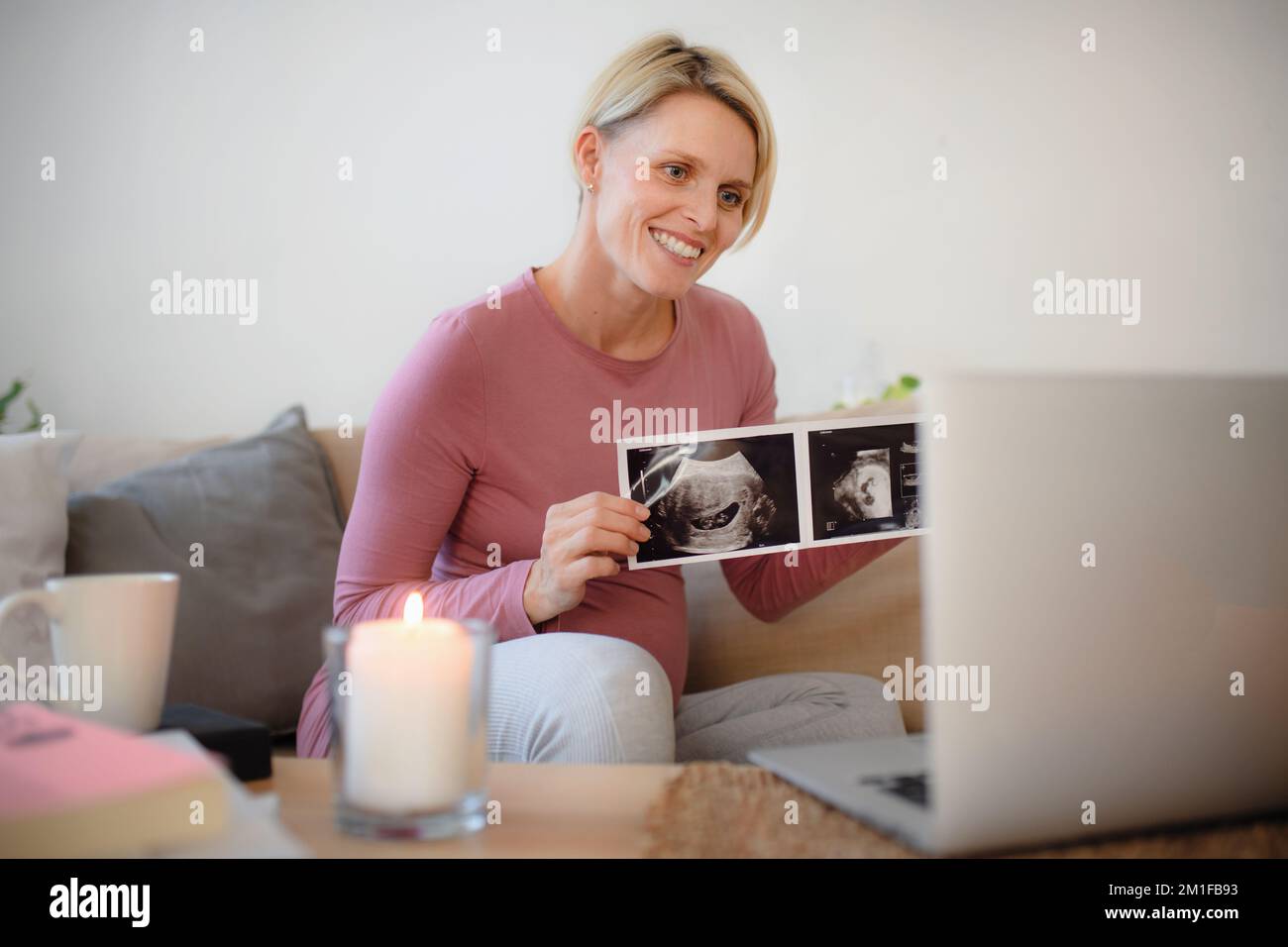 Pregnant woman showing ultrasound photo of her baby to webcam. Stock Photo