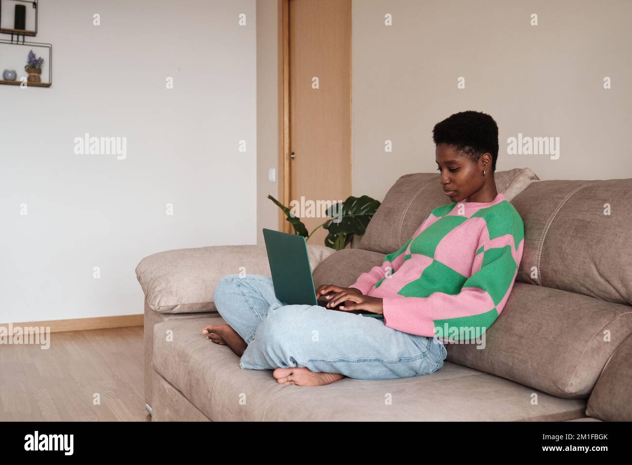 Black female freelancer using laptop while sitting on sofa Stock Photo