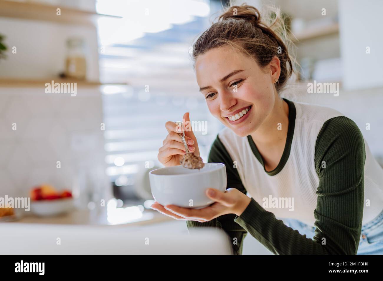 Young woman having muesli for breakfast in her kitchen, morning routine and healthy lifestyle concept. Stock Photo