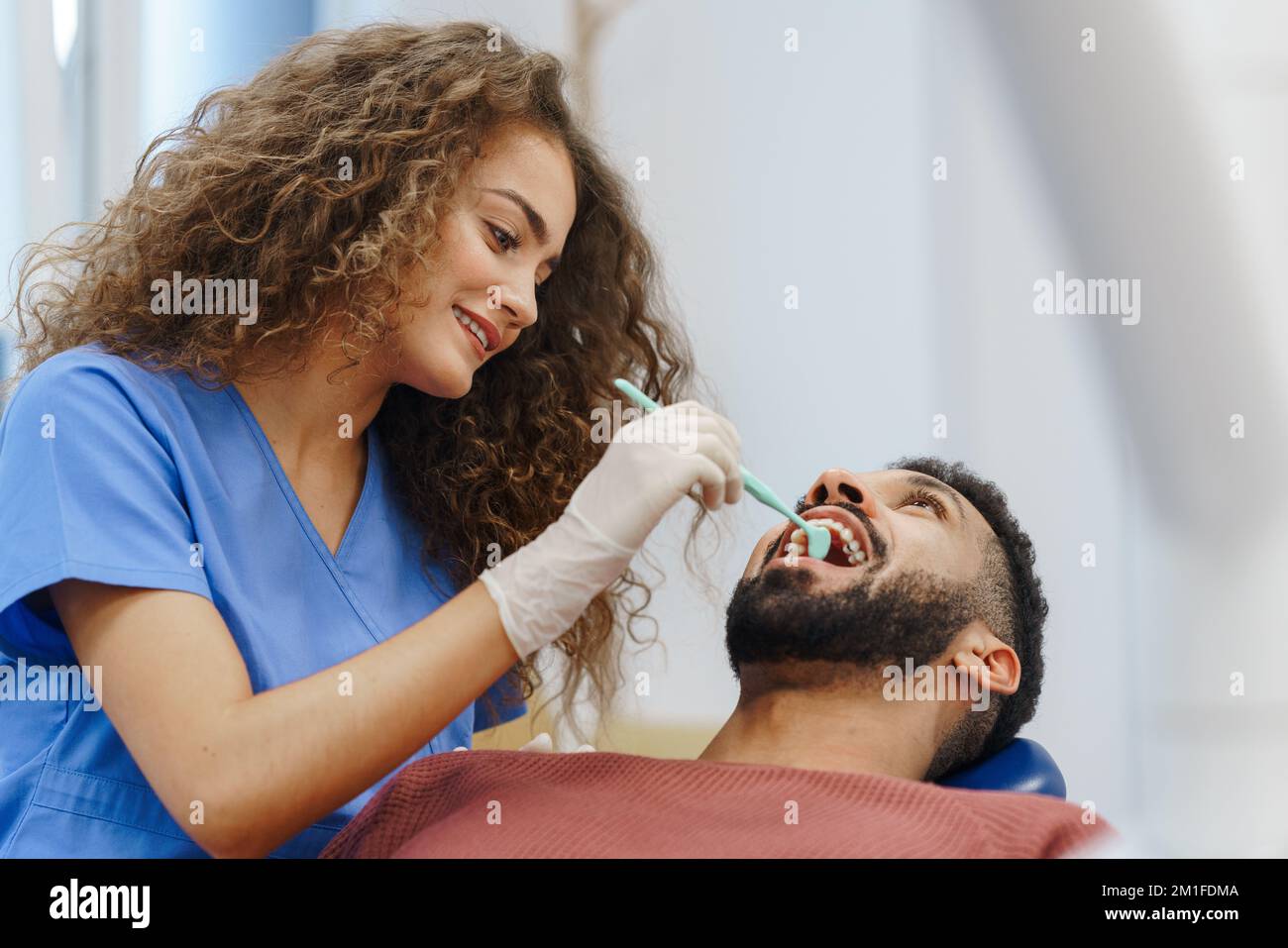 Young woman dentist doing doing preventive examination to multiracial man. Stock Photo