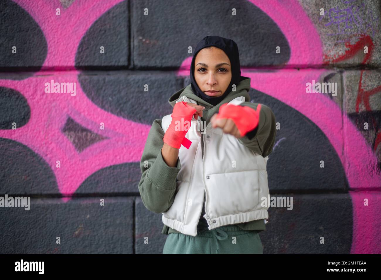 Portrait of young muslim woman with sports gloves, standing in front of graffiti. Stock Photo