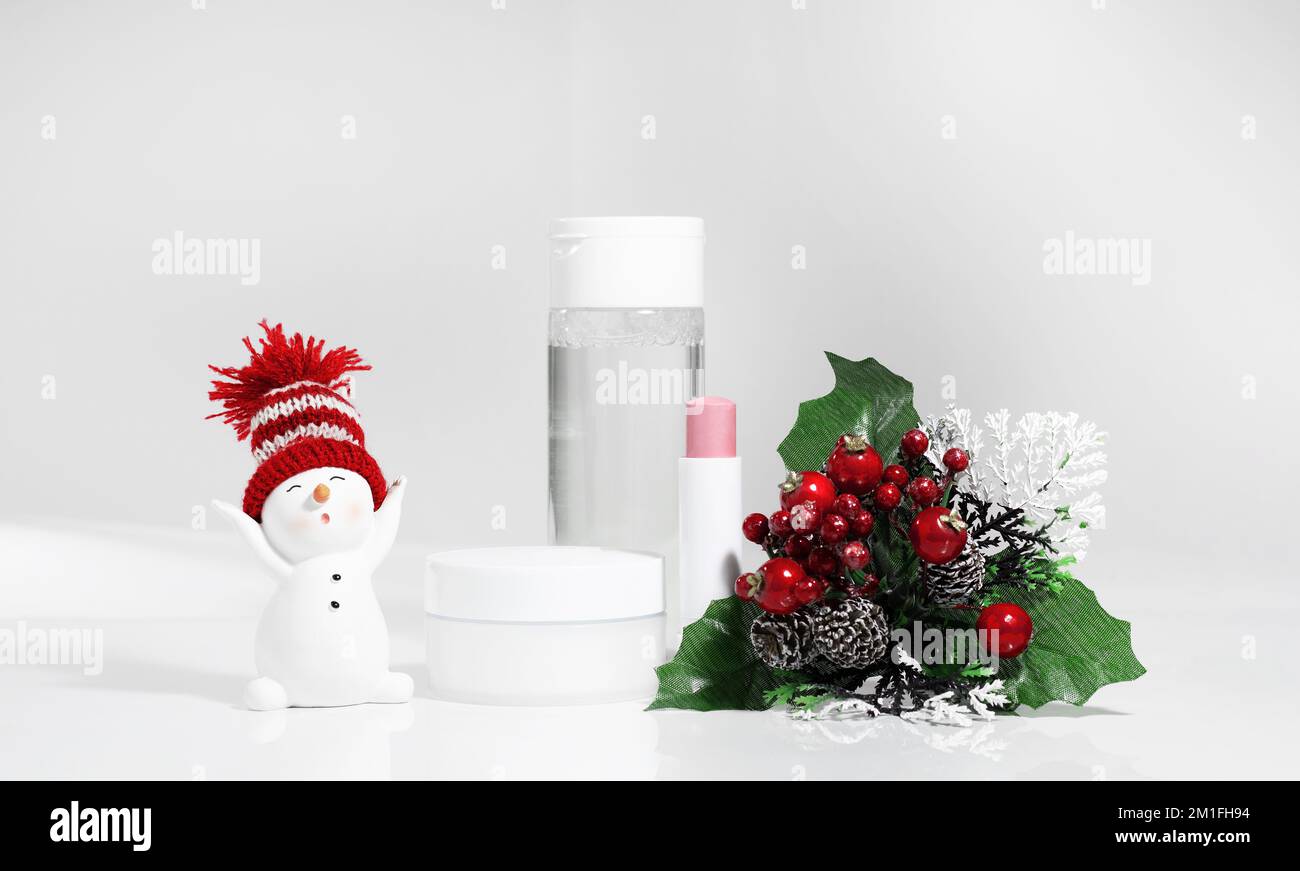 Skincare cosmetics bottles on white surface whith snowman. Winter season cosmetics. Blank containers with gifts and fir twigs backdrop. Christmas pres Stock Photo