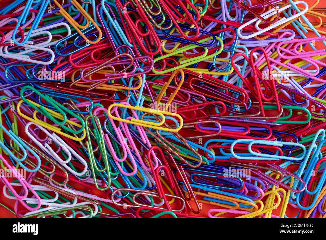 random stack of mutli colored wire plastic coated paper clips on a red background Stock Photo