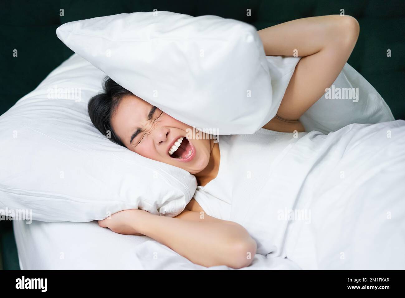 Sad girl with insomnia. Young asian woman lying in bed, cover her ears