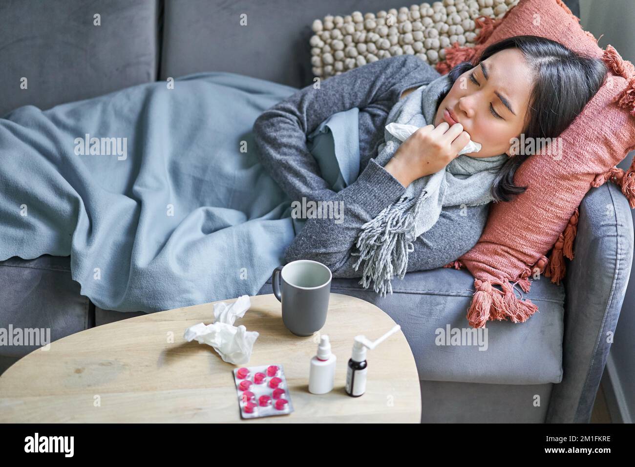 Sick sad korean woman lying on sofa, feeling unwell, catching cold, flu