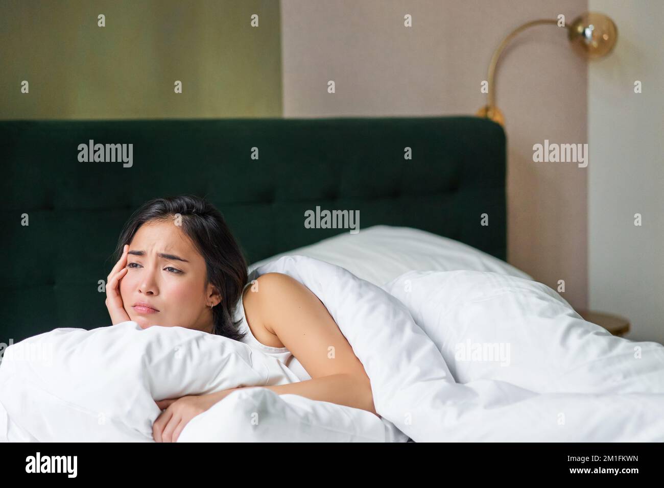 Sad and distressed young korean woman lying in her bed with pillow and ...