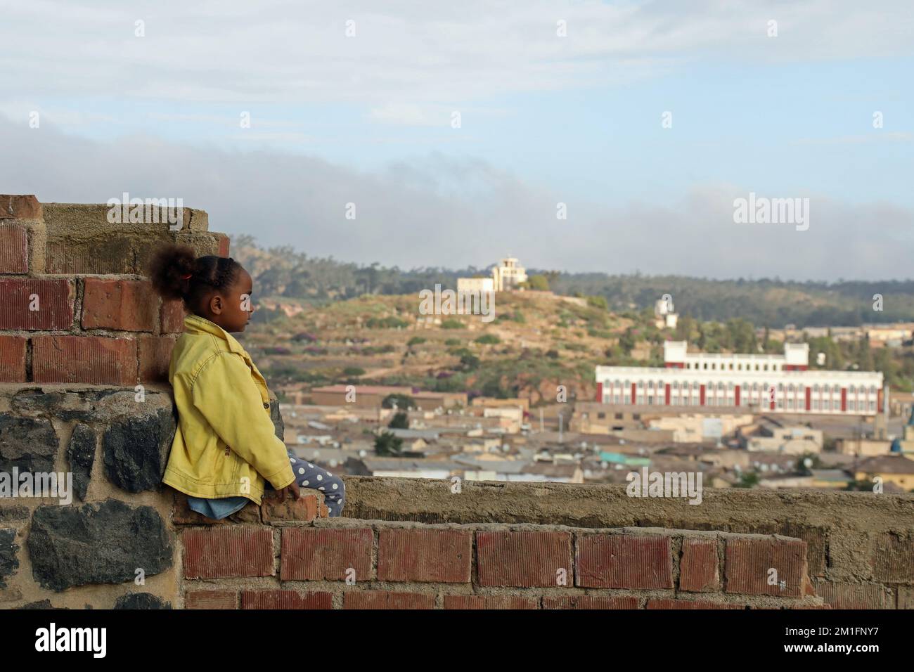 Local girl sitting on a wall overlooking the city of Asmara in Eritrea Stock Photo
