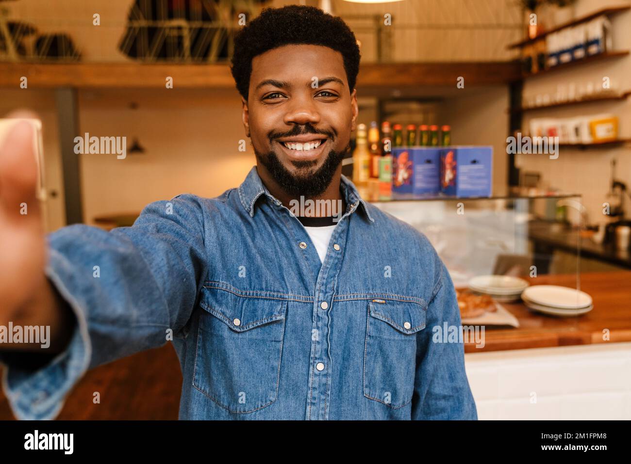 Black bearded man smiling while taking selfie photo in cafe indoors Stock Photo