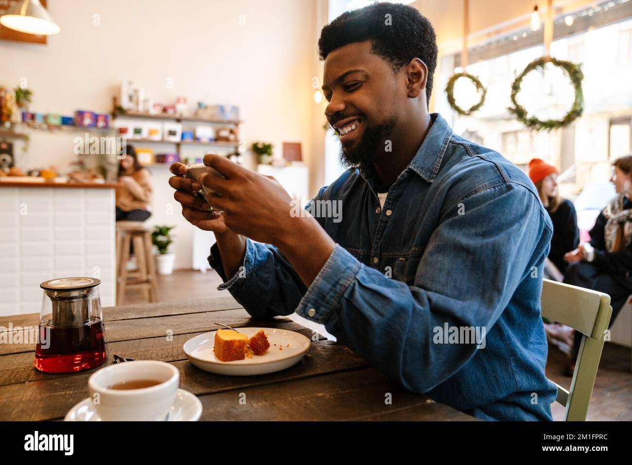 Black smiling man using mobile phone while having brunch in cafe indoors Stock Photo