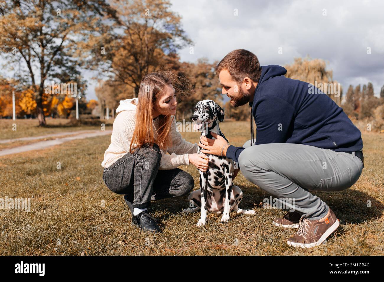 A young couple is having fun with a Dalmatian dog outdoors. Stock Photo