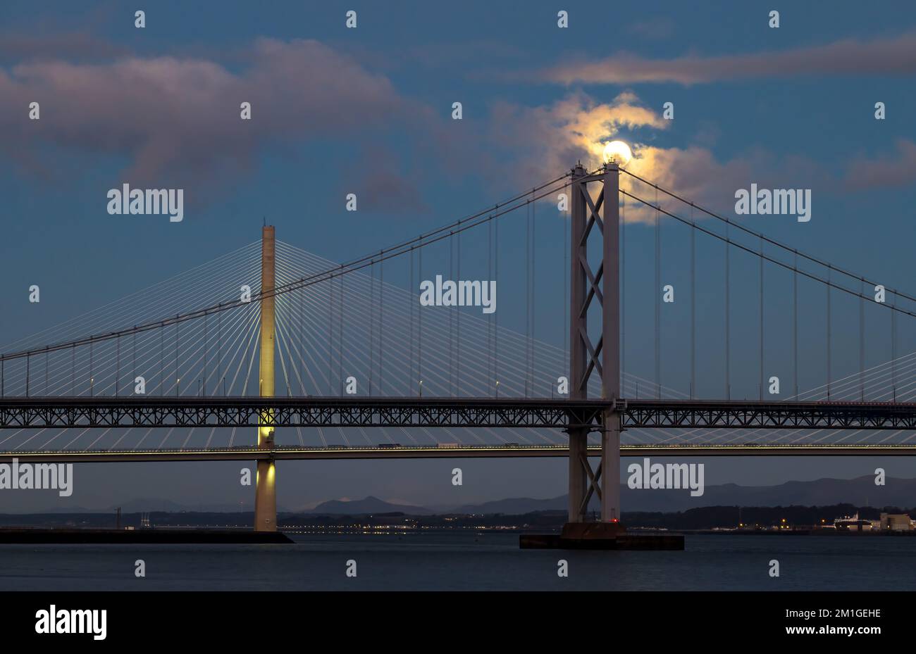 A full moon sets over Queensferry Crossing and Forth Road bridges in blue hour, Firth of Forth, Scotland, UK Stock Photo