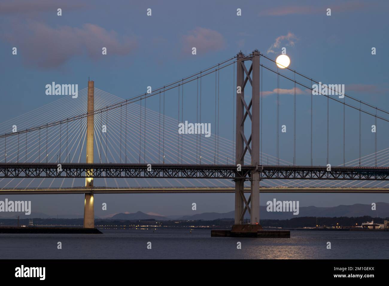 A full moon sets over Queensferry Crossing and Forth Road bridges in blue hour, Firth of Forth, Scotland, UK Stock Photo