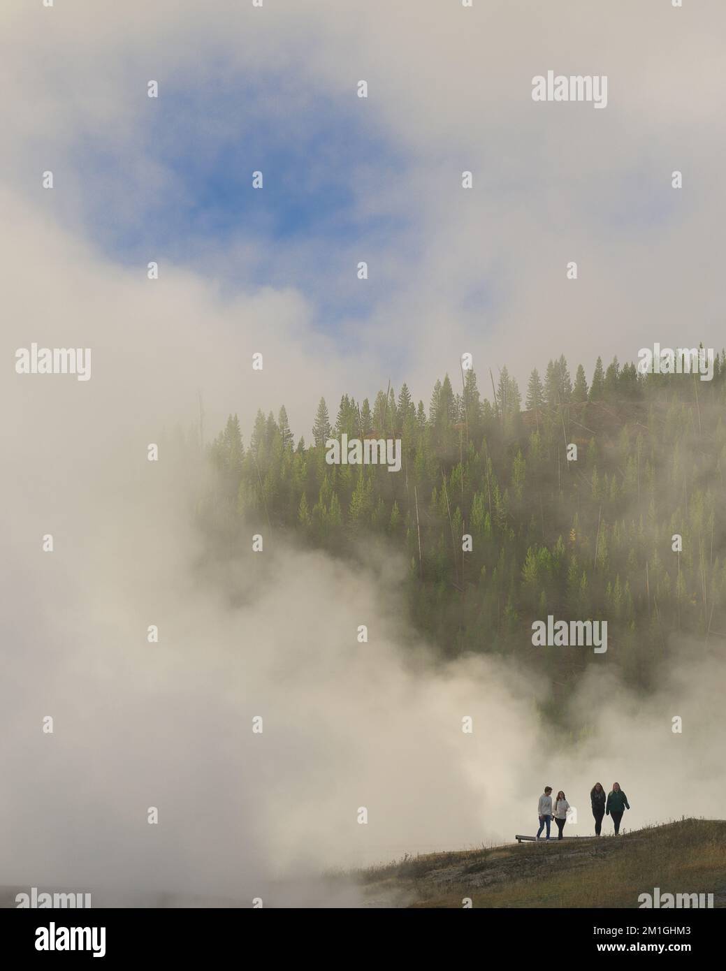 Four tourists below steamy tree line at the Midway Geyser Basin of Yellowstone National Park, Wyoming Stock Photo
