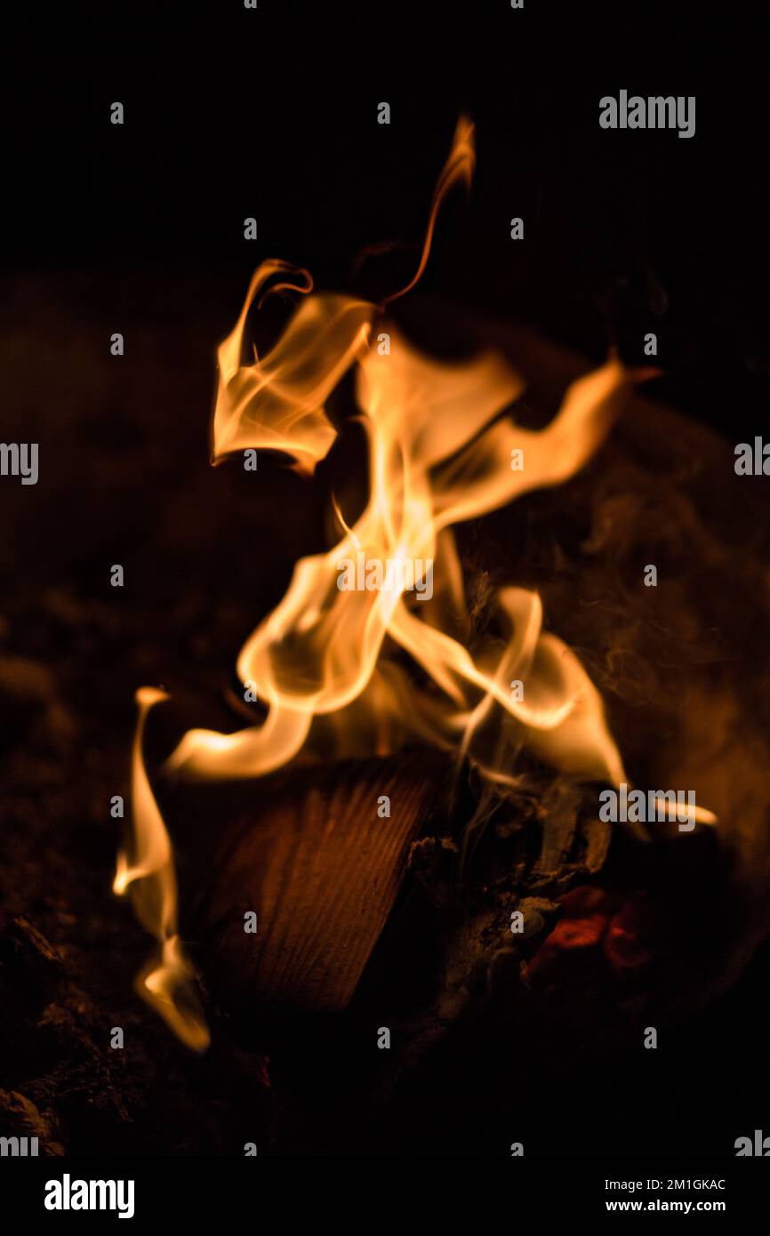 A closeup of a bonfire with flames of orange-yellow and smoke at night ...
