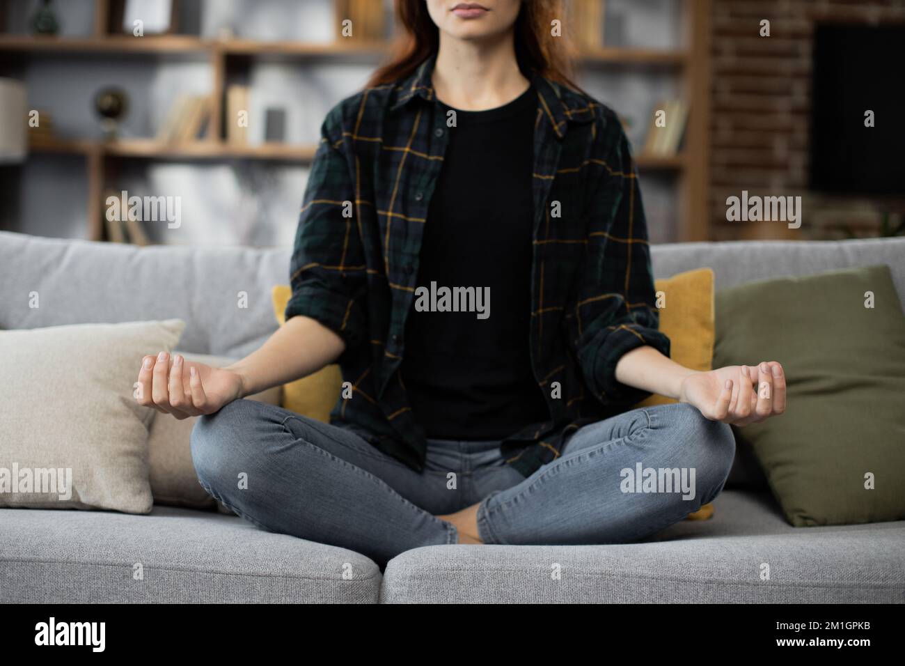 Cropped view Yong female sitting on couch in lotus pose put hands on lap folded fingers enjoy meditation do yoga exercise at home. No stress healthy habit mindfulness lifestyle anxiety relief concept Stock Photo