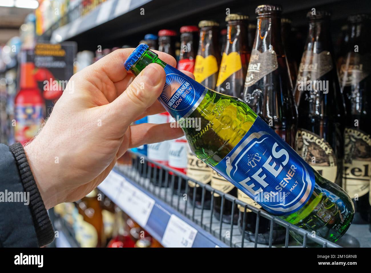 Man's hand is holding Efes beer bottle from supermarket shelf. Various bottles of beer on shelf in store. Minsk, Belarus, 2022 Stock Photo