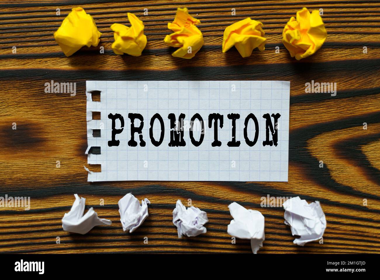 Business and finance concept. On a wooden board lie crumpled leaves of paper and a sheet from a notebook on which it is written - PROMOTION Stock Photo