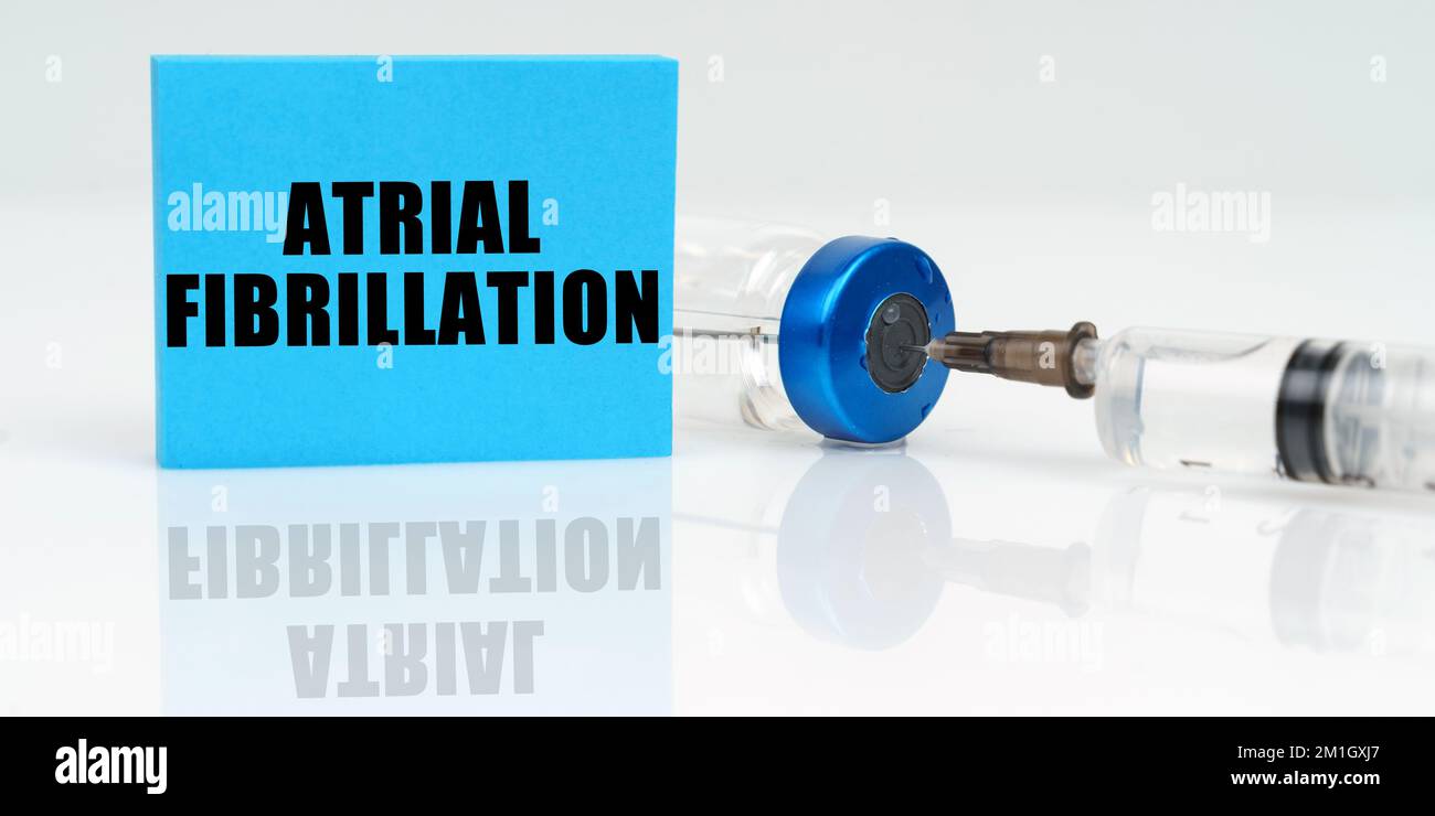 Medicine concept. On a white reflective surface are a syringe, an injection and a blue plaque that says - Atrial Fibrillation Stock Photo