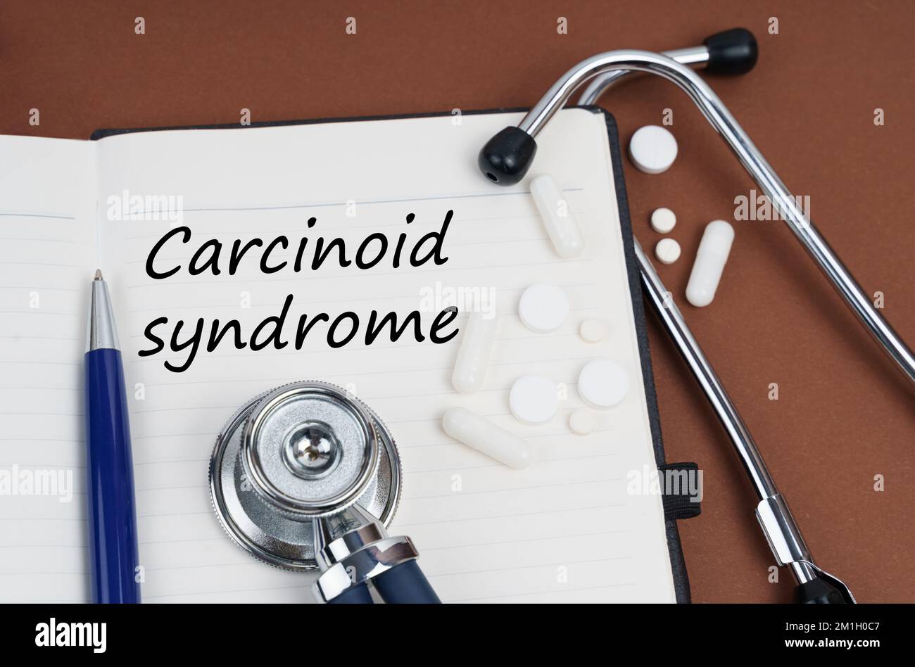 Medicine and health concept. On a brown surface lie pills, a pen, a stethoscope and a notebook with the inscription - Carcinoid syndrome Stock Photo