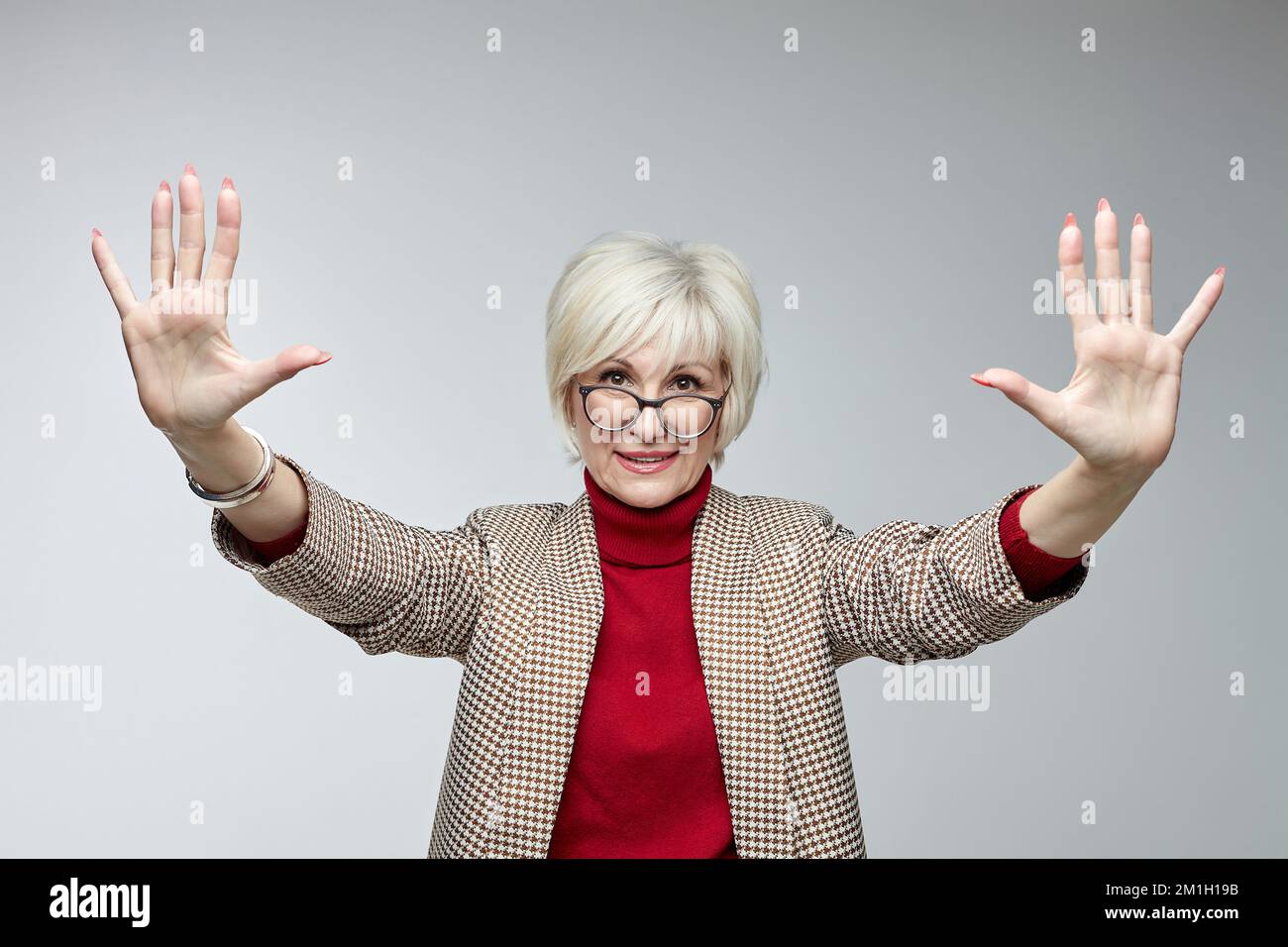 beautiful elderly woman with glasses holds her hands in front of her with open palms facing the camera. advertising concept of a business woman leader Stock Photo