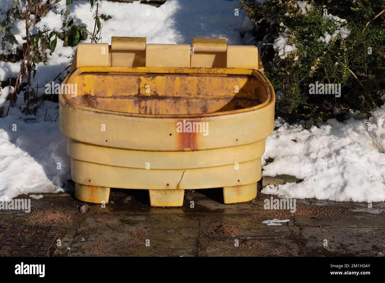 Empty yellow salt and grit bin. snow on the ground and rusty bin with