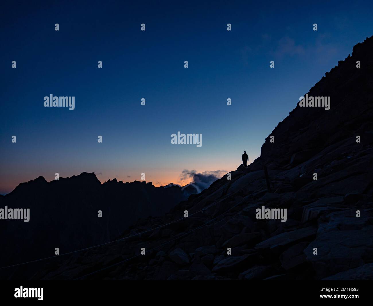 Silhouette of a mountaineer tourist with a headlamp on a ridge during colorful sunset, fearless determination courage, Tatra mountains Slovakia Vysoke Stock Photo