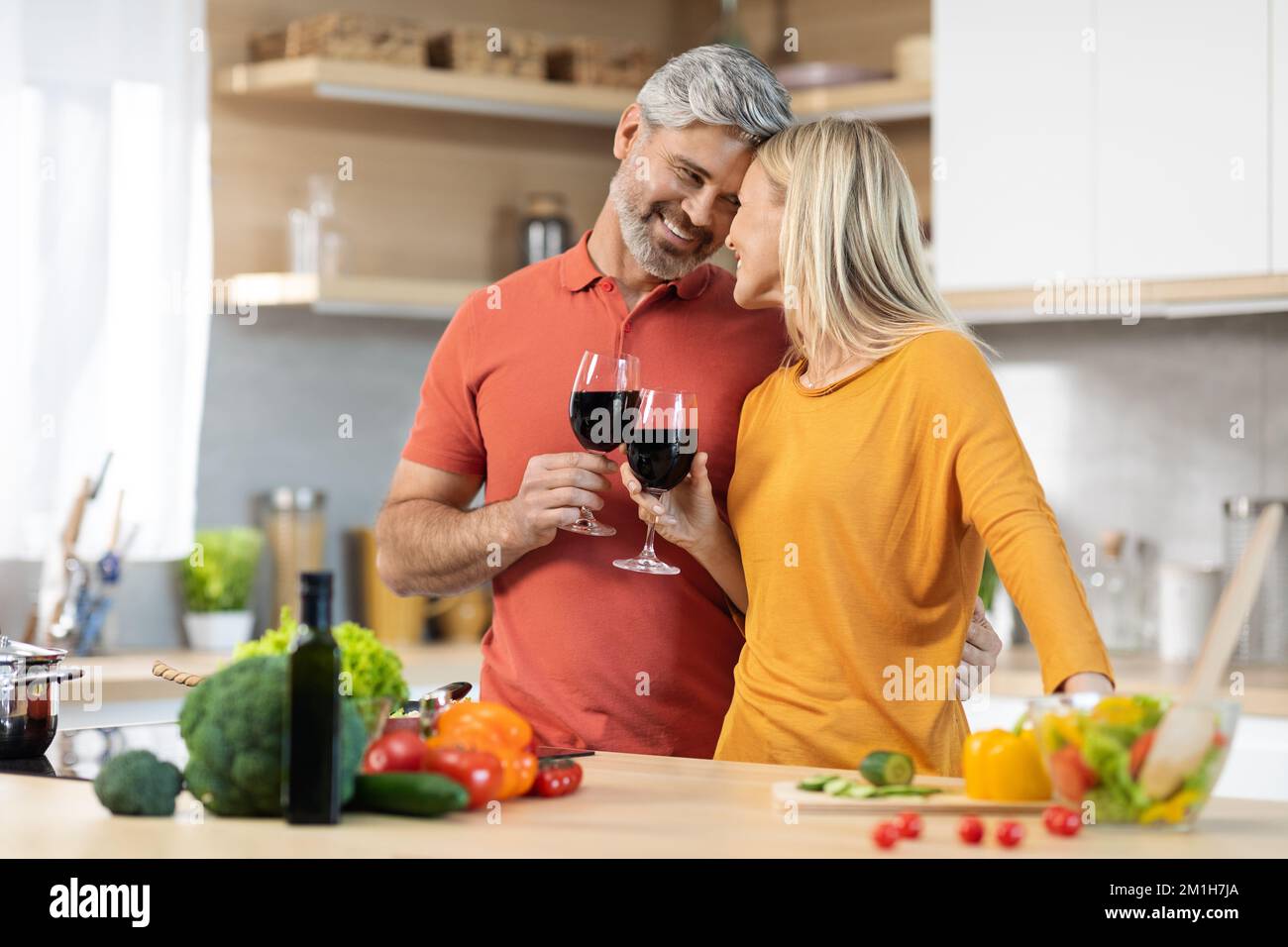 Bonding mature couple drinking wine while preparing dinner Stock Photo