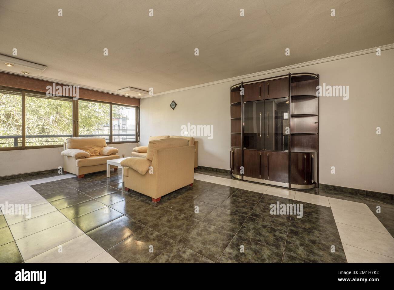 Living room with two-tone stoneware floors, a wall-to-wall window, a fabric lounge set, and old furniture Stock Photo