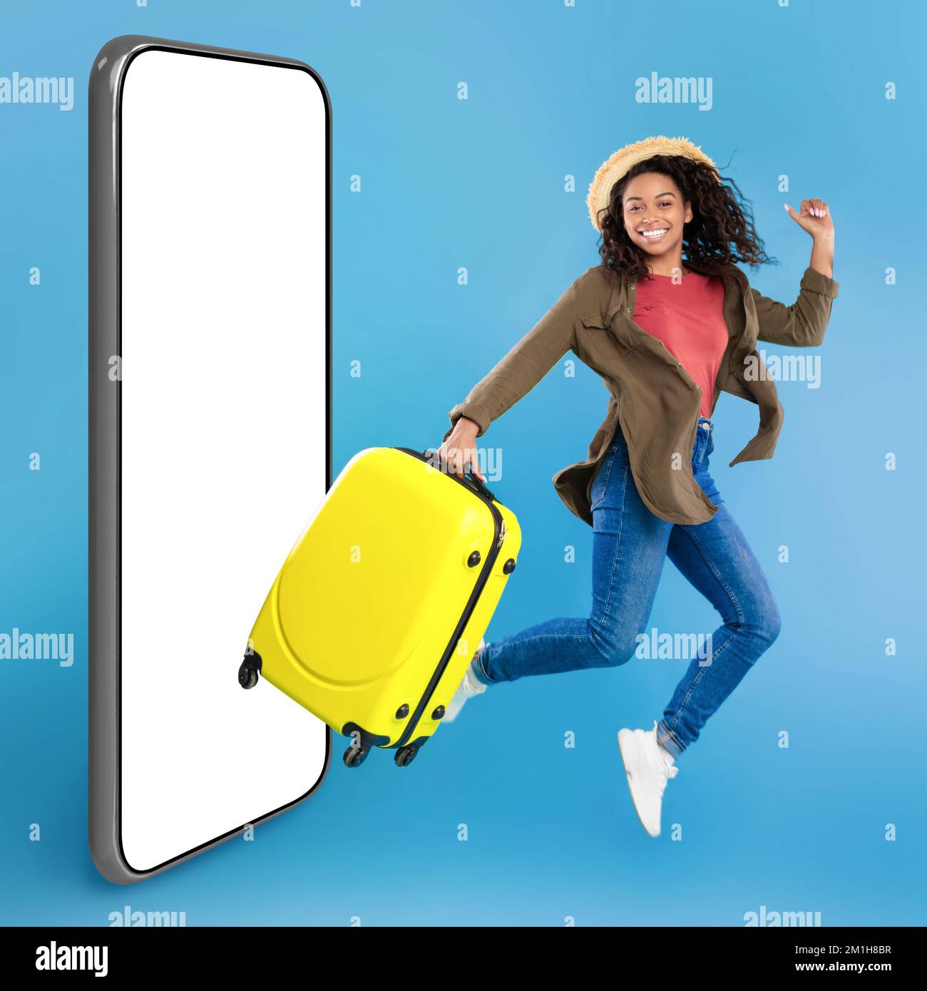 Excited young black woman in casual wear with bright suitcase jumping on blue studio background