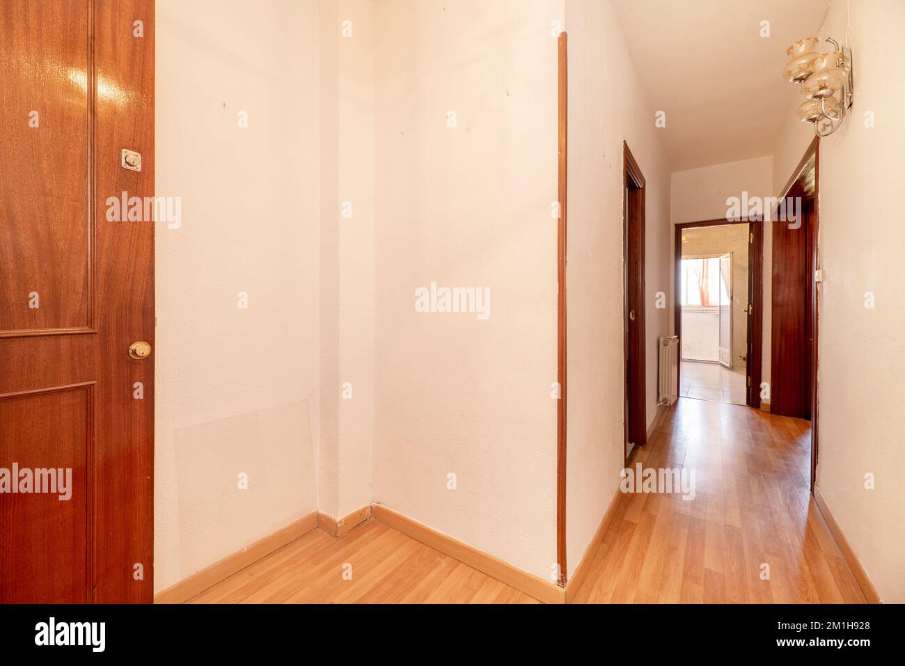 Lobby of a house with a solid wood access door, laminated flooring and sconces with crystal lampshades Stock Photo
