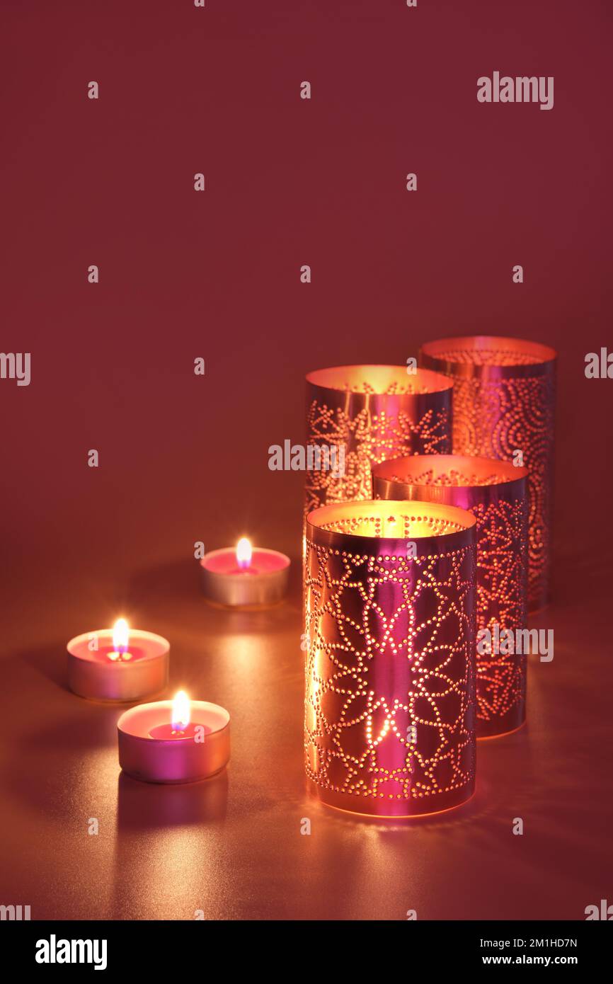 Oriental metal lanterns and tea lights. Dark red, magenta, brown and golden monochromatic background. Stock Photo
