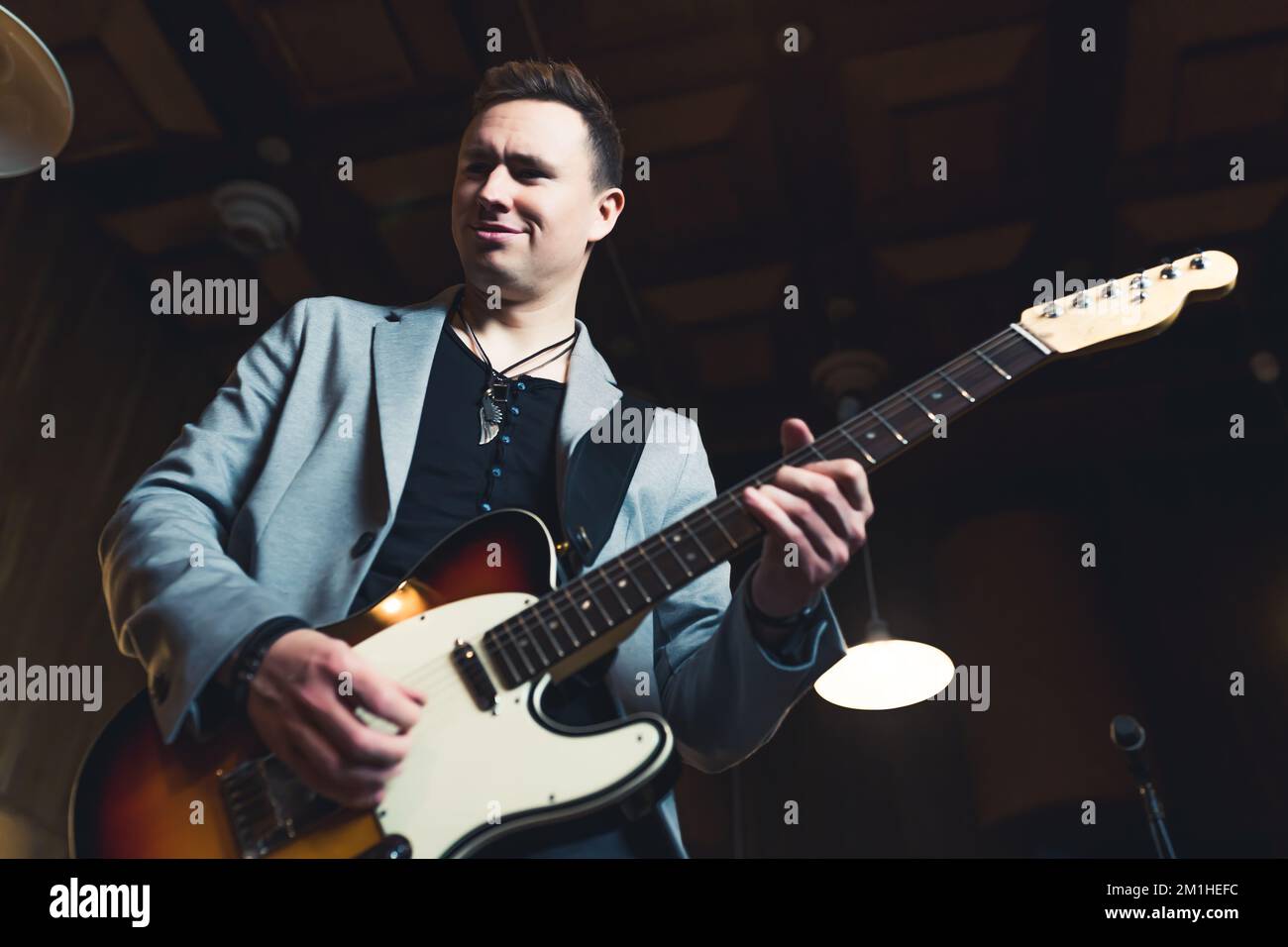 Musician playing on a guitar. Caucasian mid adult man in a rock band playing his guitar. Stage lightening. Low angle indoor shot. High quality photo Stock Photo